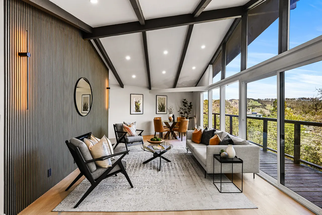 Living room with a slatted wood wall, dark beams and a wall of glass onto a cable-rail deck