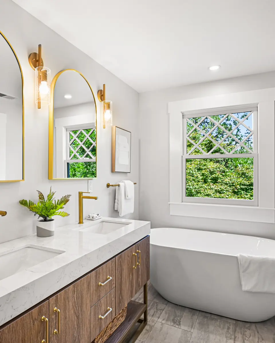 Bath with a freestanding tub, brass fixtures and arched mirrors
