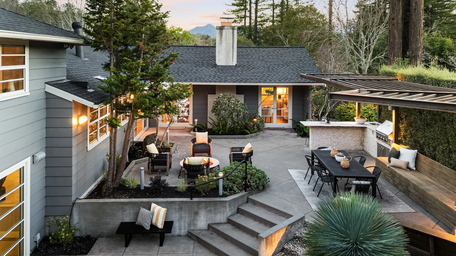 A courtyard at dusk with a fire pit, outdoor dining and hills beyond