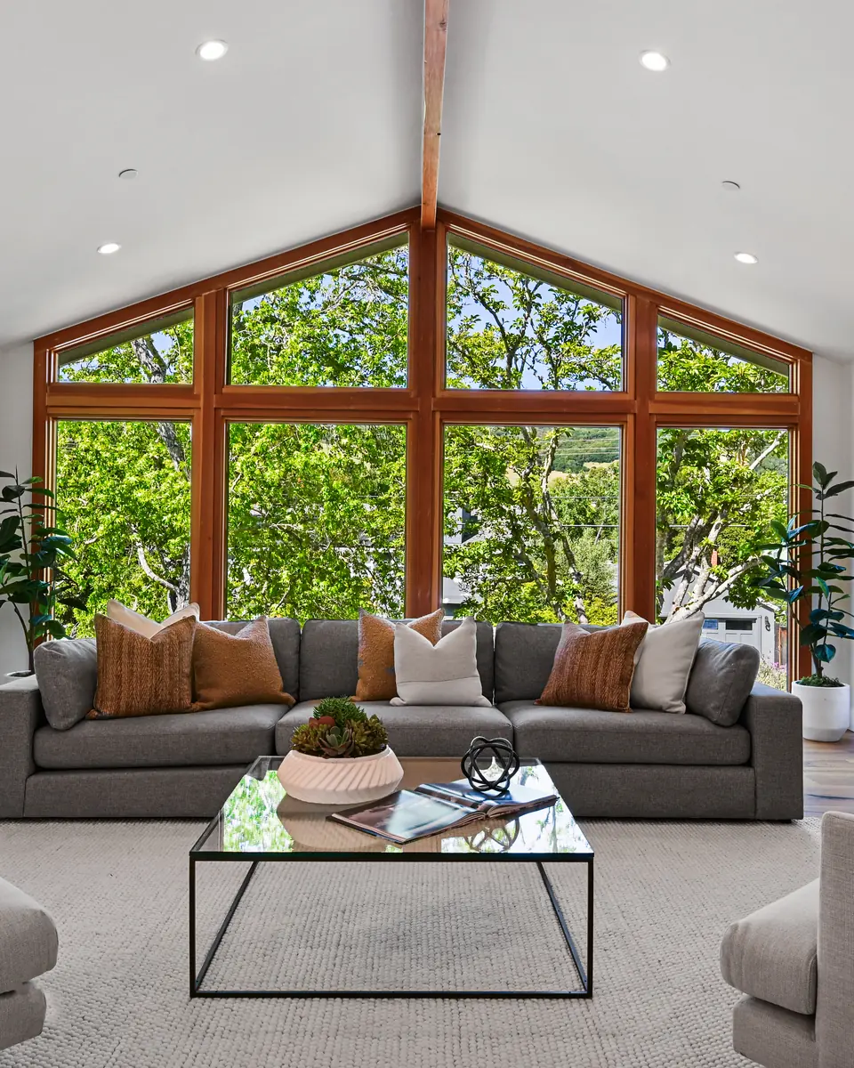 Living room under a vaulted ceiling, with a wall of wood-framed windows onto the trees