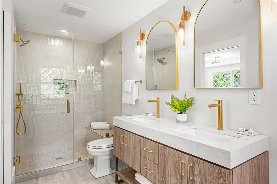 Bath with a glass shower, a double vanity and arched brass mirrors