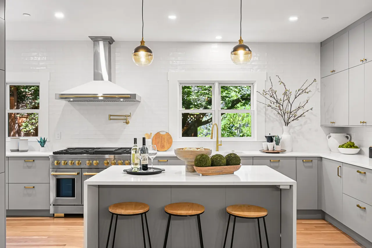 Kitchen with a white island, wood stools, glass globe pendants and a range under a steel hood