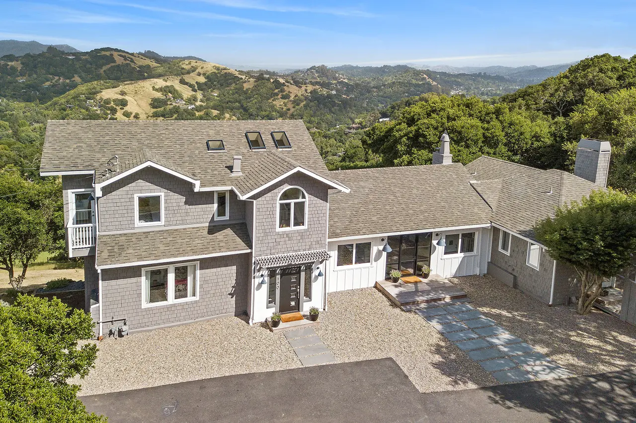 Aerial view of a gray shingle home, with oak-covered hills behind it